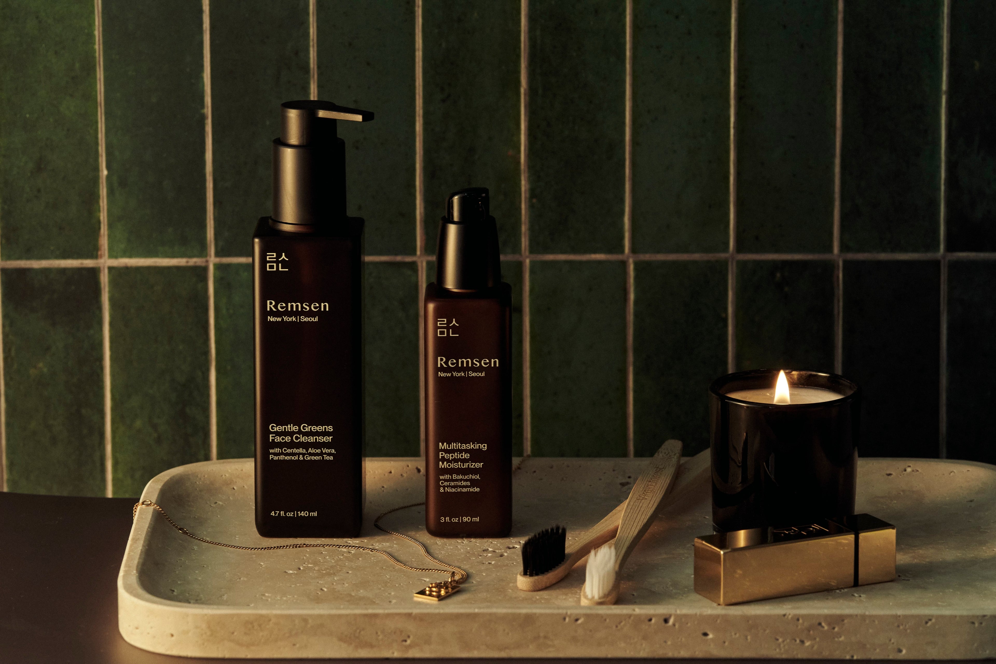 Two bottles of Remsen products on a stone tray with a lit candle against a tiled wall background.